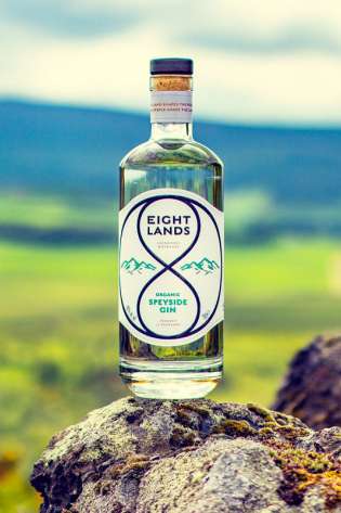 Eight Lands Organic Gin bottle on rock with hill backdrop.