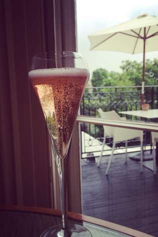 Champagne flute with rosé on a table; outdoor patio visible through a window.