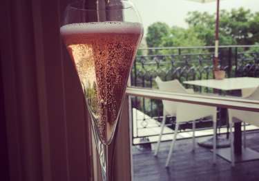 Champagne flute with rosé on a table; outdoor patio visible through a window.
