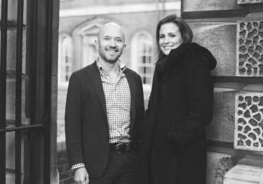 Two people stand smiling in a black-and-white photo.