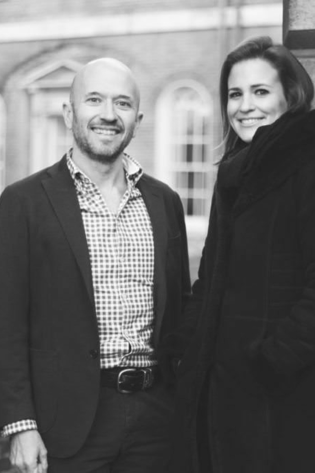 Two people stand smiling in a black-and-white photo