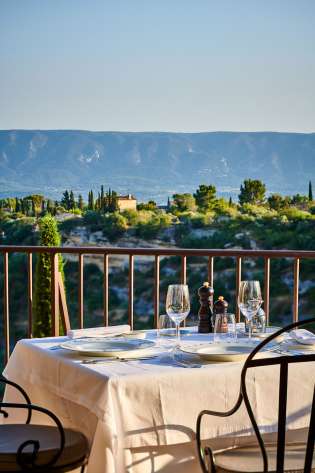 A table set with white tablecloth and glassware overlooks a scenic landscape of lush greenery and mountains under a clear blue sky.