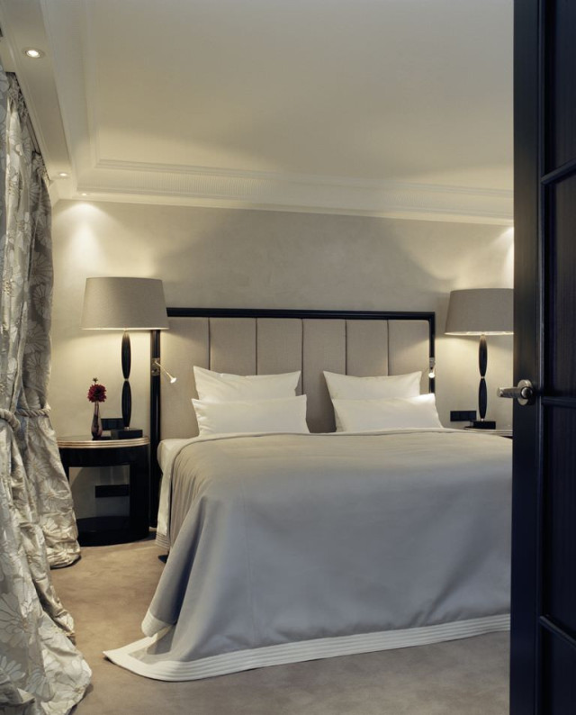 A neatly made bed with a gray cover stands between two tall lamps
