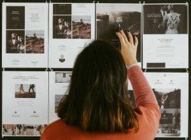 A person in a red shirt reaches towards images pinned on a wall