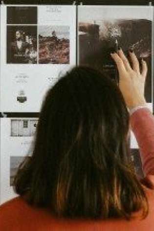 A person in a red shirt reaches towards images pinned on a wall.