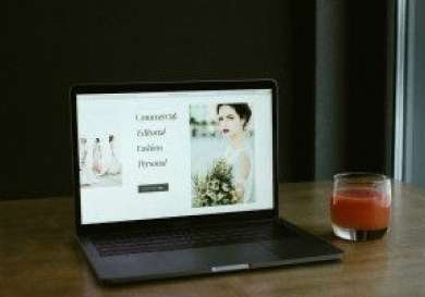 A laptop displays a photography website with text: