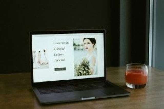 A laptop displays a photography website with text: