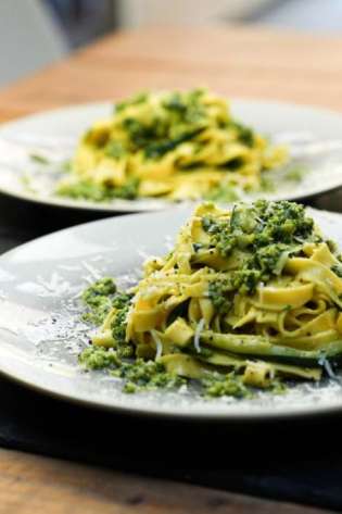 Pasta covered in green pesto sauce sits on a white plate.