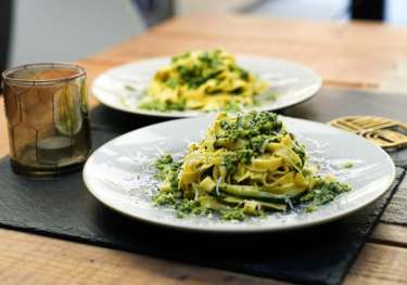 Pasta covered in green pesto sauce sits on a white plate.