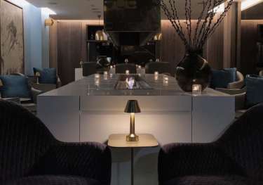 Purple armchairs flank a brass table in a lounge area.