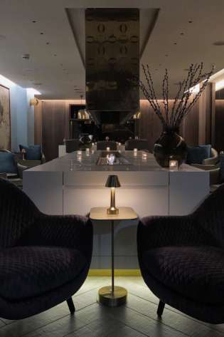 Purple armchairs flank a brass table in a lounge area.