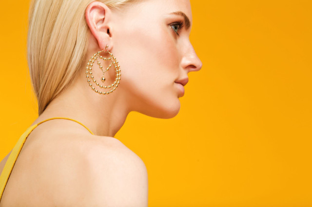 A woman faces sideways wearing large, intricate hoop earrings with beads
