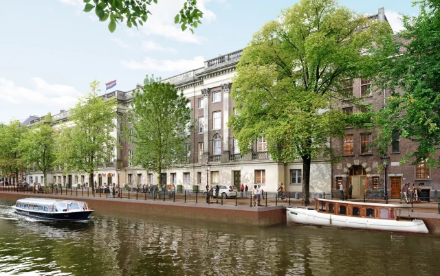 Canal-side building with lush trees, boats, and people strolling.