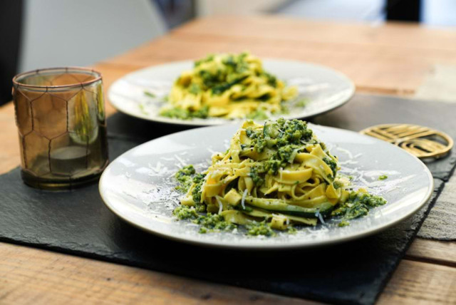 Pasta covered in green pesto sauce sits on a white plate