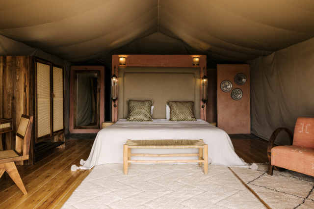 Bed inside canvas tent with wooden furniture.