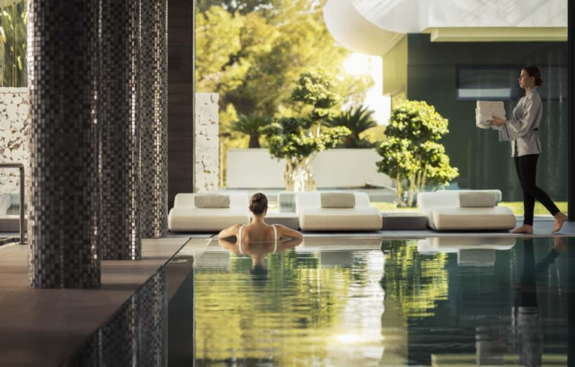 Woman in indoor pool at luxurious spa; staff nearby.