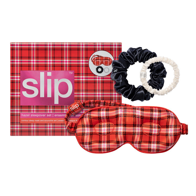 A red plaid sleep mask and black and cream scrunchies rest on matching plaid packaging labeled
