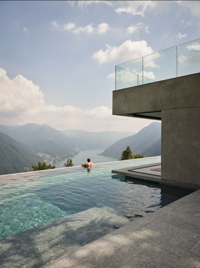 Man in an infinity pool overlooking a lake and mountains.