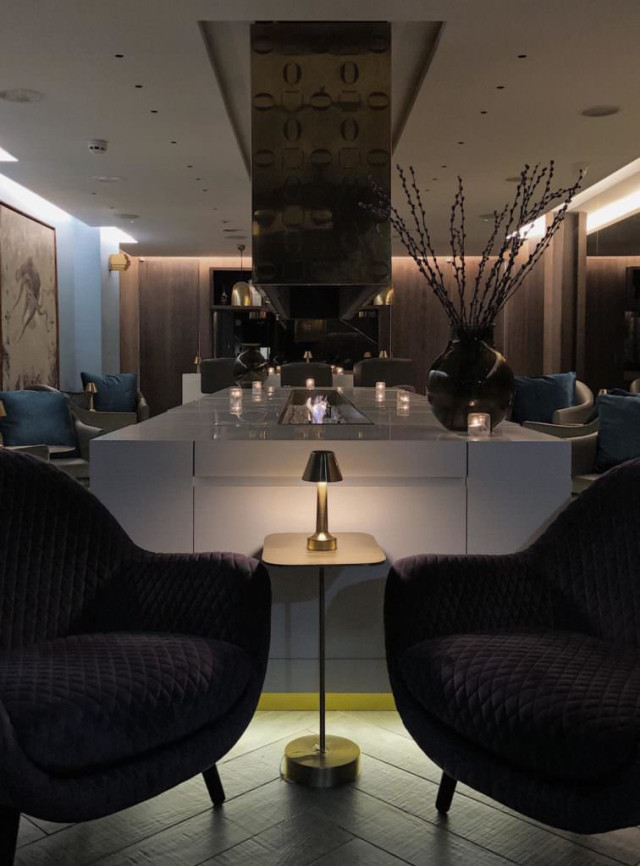 Purple armchairs flank a brass table in a lounge area.